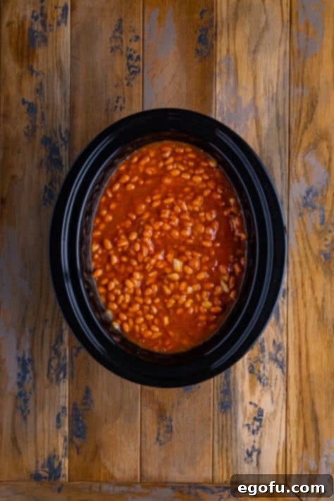 The slow cooker, covered with its lid, working its magic as the baked beans simmer gently on a low setting.