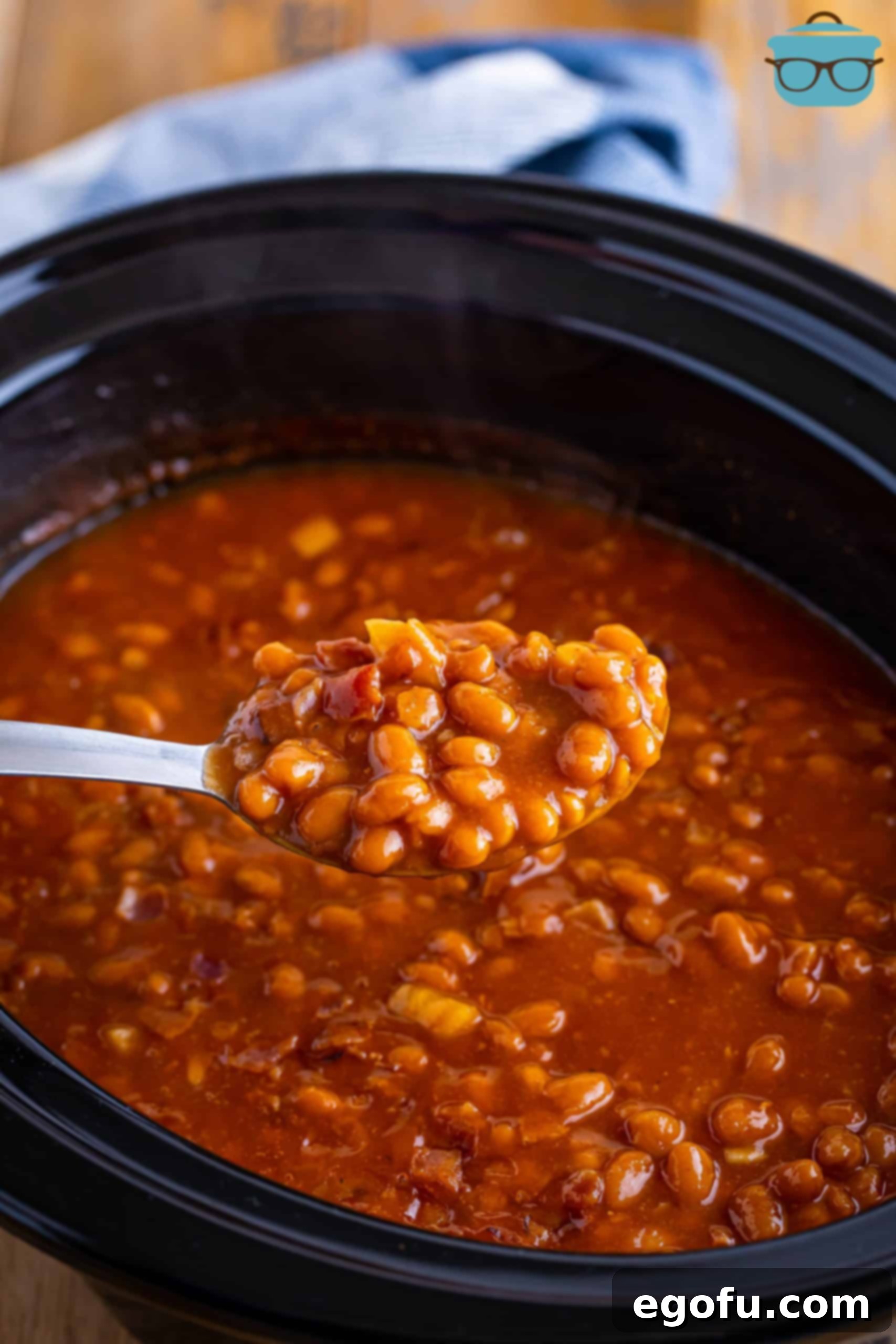 A serving spoon capturing a generous scoop of the finished, perfectly cooked Crock Pot Baked Beans, showcasing their rich color and inviting texture.