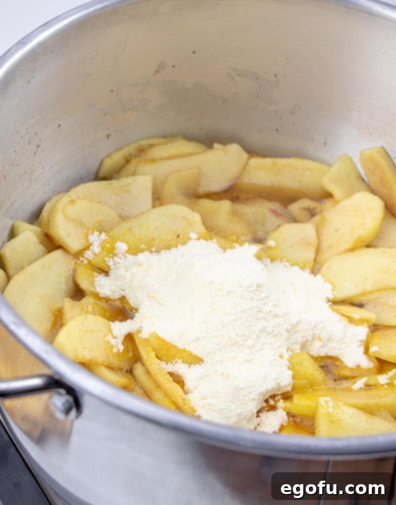 The simmering apple mixture in a large saucepan, with the remaining water and Cook & Serve vanilla pudding mix just added, beginning to thicken into a delicious apple pie filling.