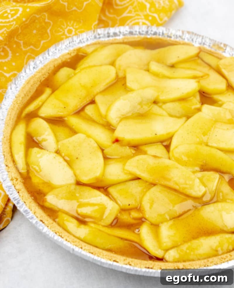 The warm no-bake apple pie filling freshly poured into a large, pre-made graham cracker crust, showing the pie ready for its essential chilling period in the refrigerator.