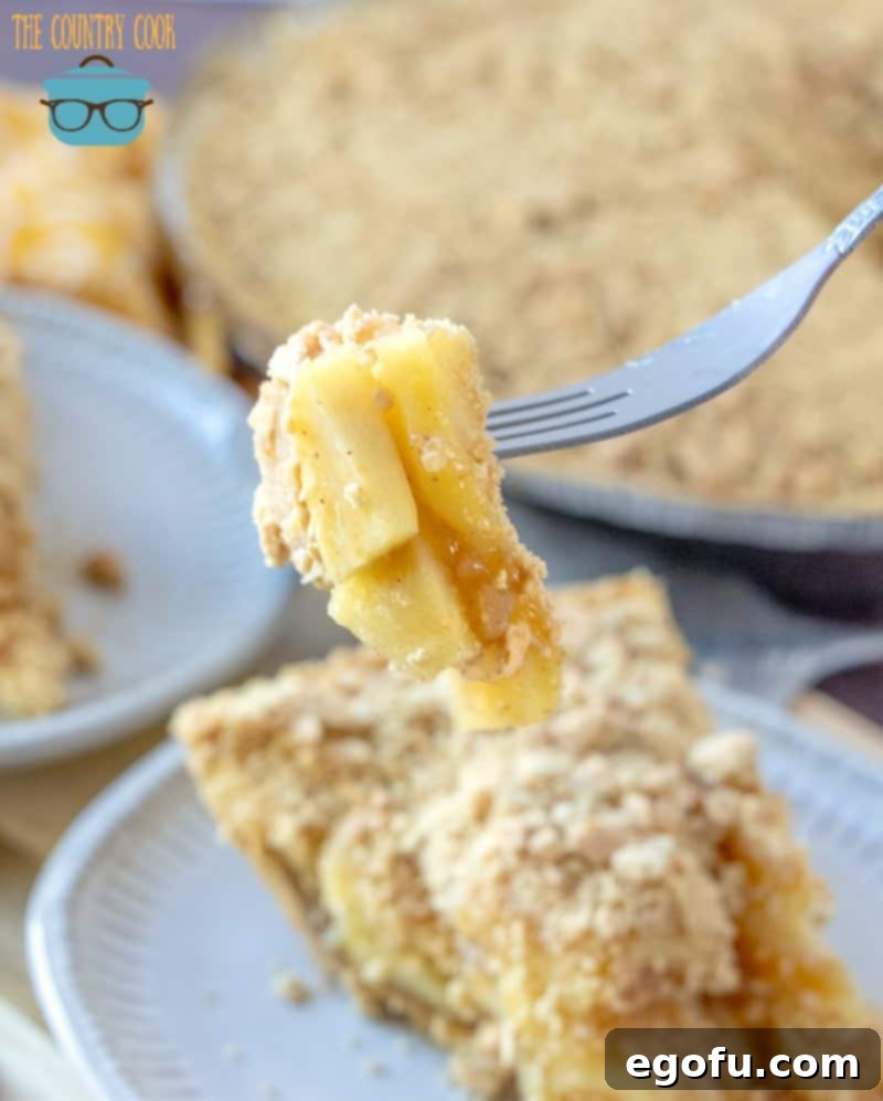 A fork holding up a perfect bite of no-bake apple pie, showcasing the tender apple filling, graham cracker crust, and crumbly topping – an inviting close-up.