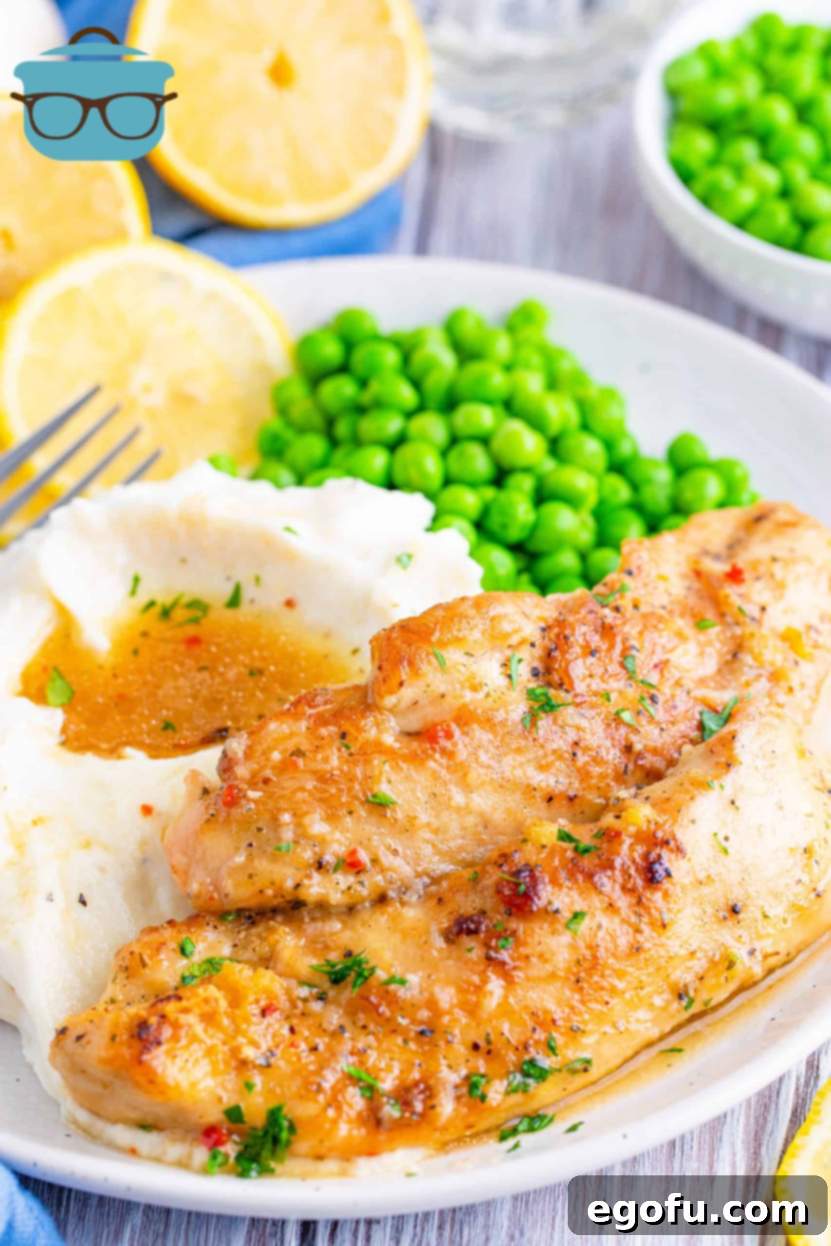 Zesty Slow Cooker Lemon Garlic Chicken 2 two slices of lemon garlic chicken tenders on a white plate with a side of mashed potatoes and peas.