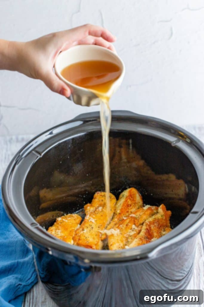 Zesty Slow Cooker Lemon Garlic Chicken 8 pouring chicken broth over chicken tenders in a slow cooker.