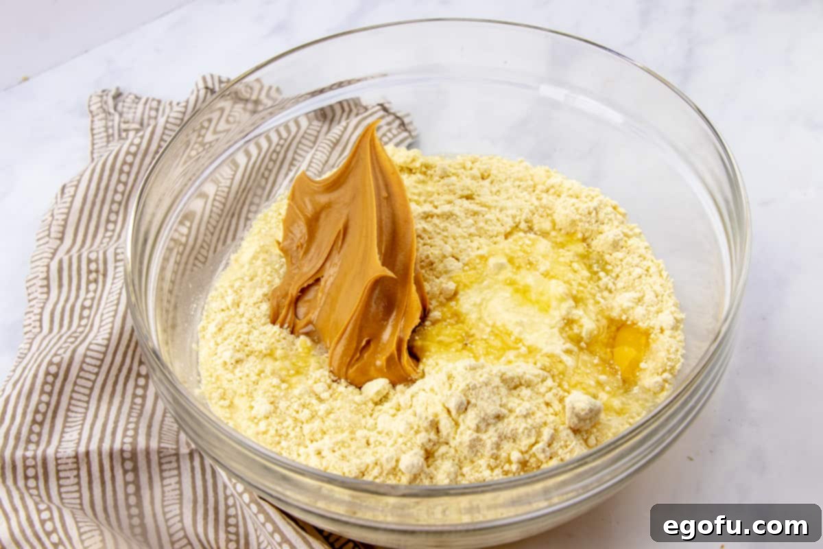 All the wet and dry ingredients including cake mix, oil, eggs, water, and creamy peanut butter, combined in a large mixing bowl, ready to be stirred into a smooth batter.