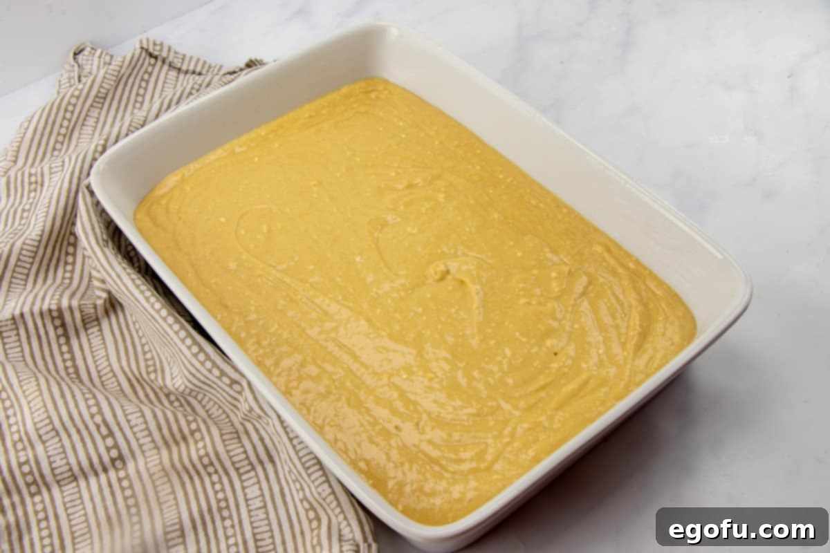 Smooth peanut butter cake batter evenly spread in a greased 9x13-inch baking dish, ready for the oven to transform into a delicious cake.