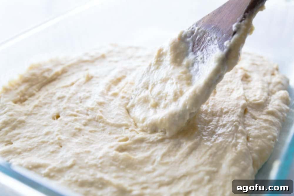 Cake mix batter being spread evenly into the bottom of a 9x13 inch baking dish.
