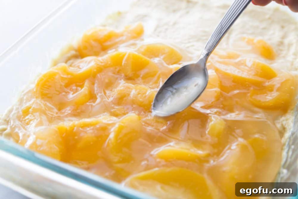 Peach pie filling being spread over the raw cake batter in a baking dish.