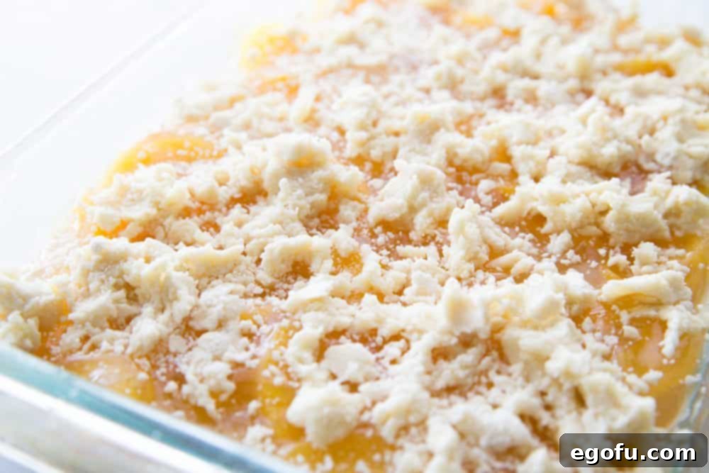 Close-up of the buttery crumble topping being sprinkled over the peach pie filling layer.