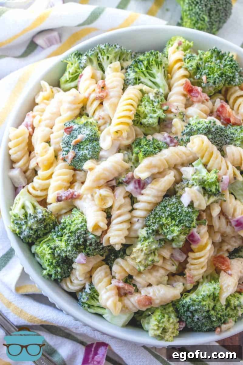 Creamy Bacon Broccoli Pasta Salad presented beautifully in a large white serving bowl, placed on a surface with a decorative white and yellow dish towel.