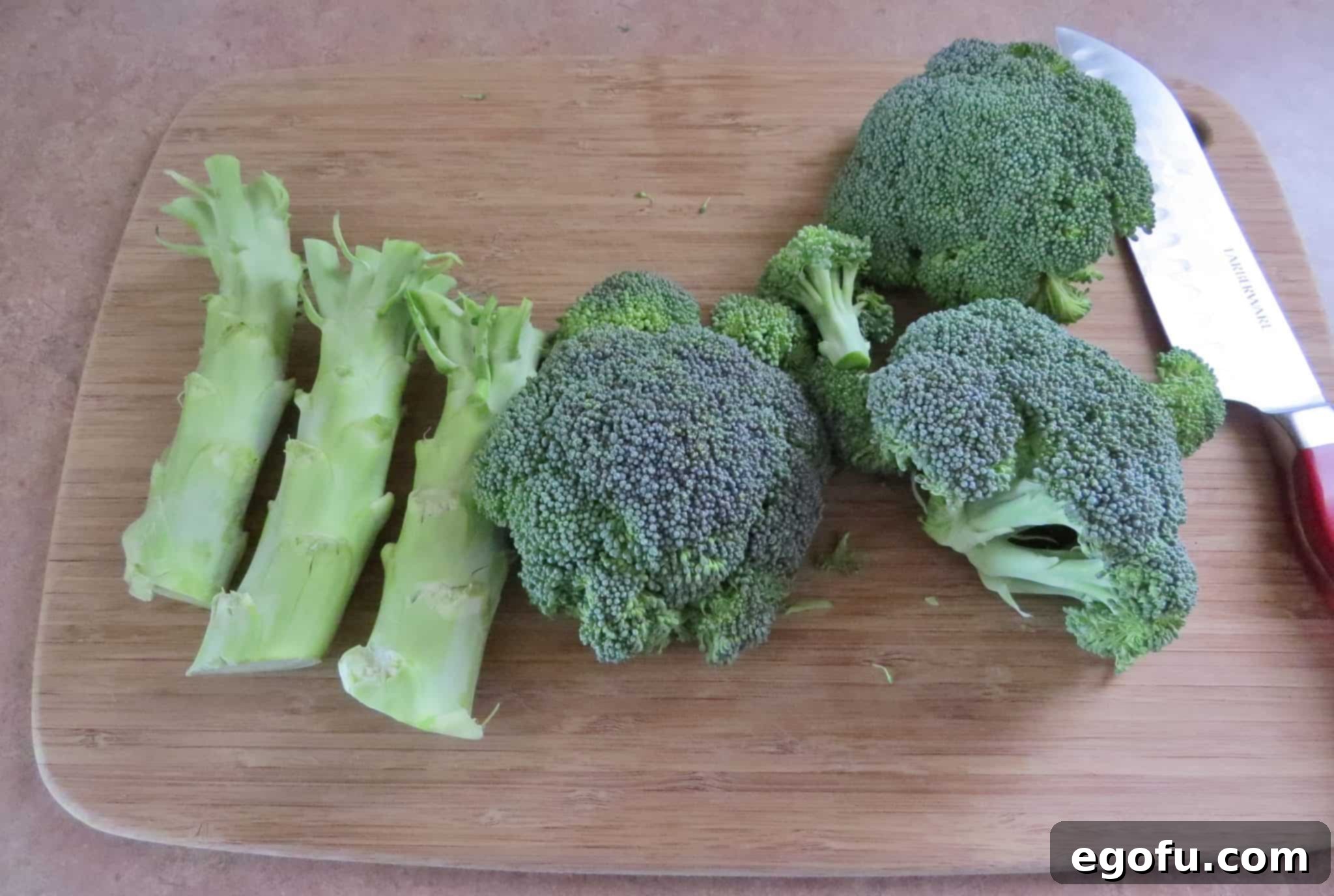 A chef's knife is shown separating fresh broccoli florets from the stem on a wooden cutting board, demonstrating how to prepare broccoli for the salad.
