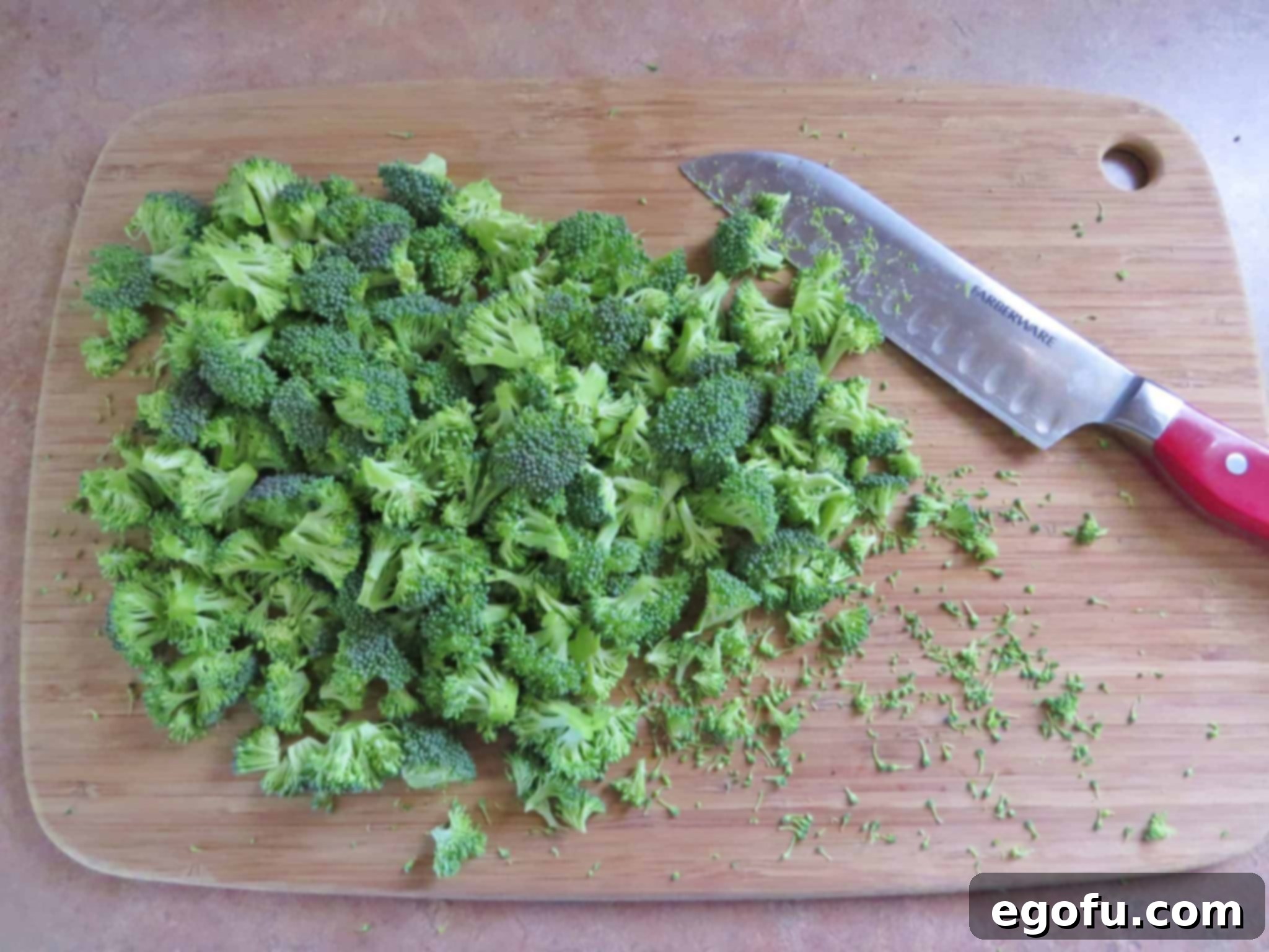 A close-up shot of perfectly chopped fresh broccoli florets laid out on a wooden cutting board, ready for the pasta salad.