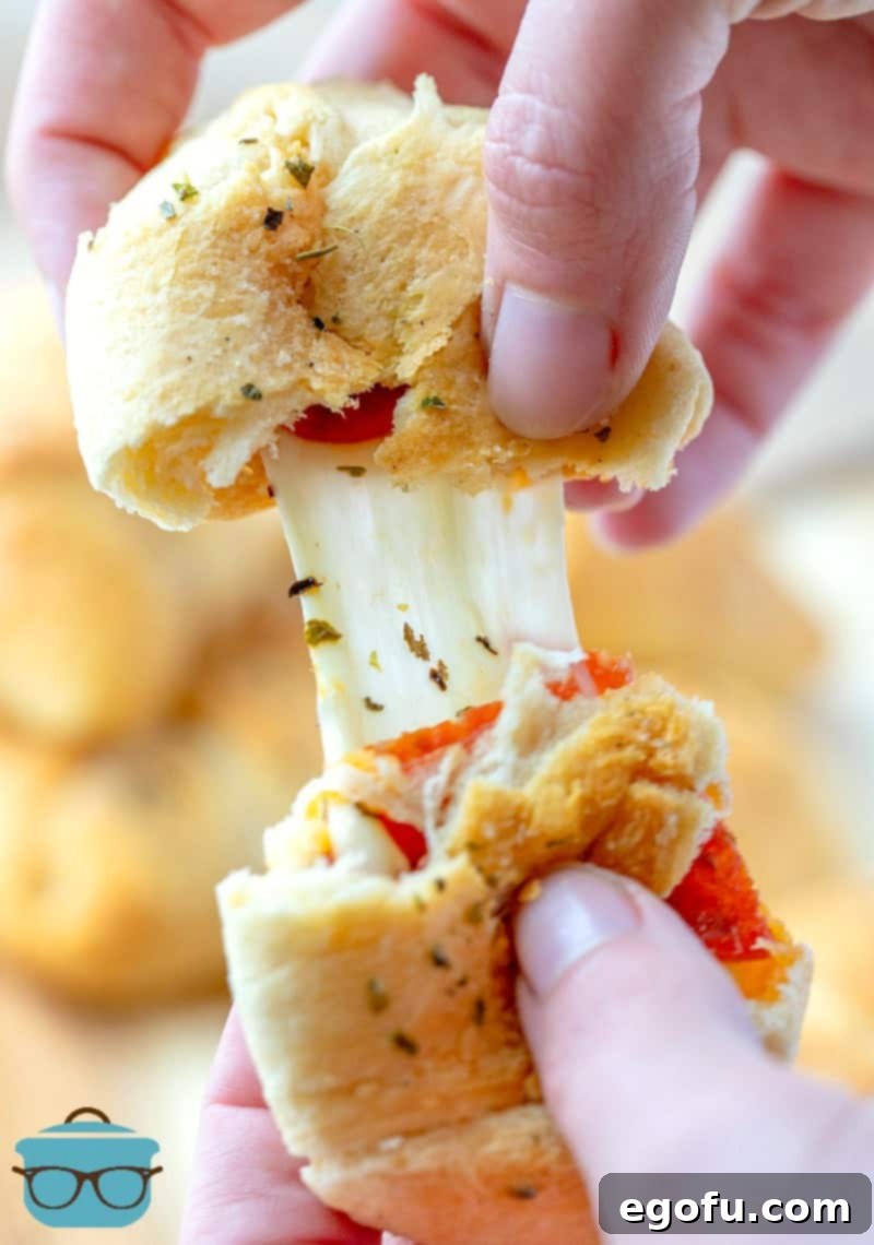 a hand pulling apart a pepperoni rollup to show the melted cheese.