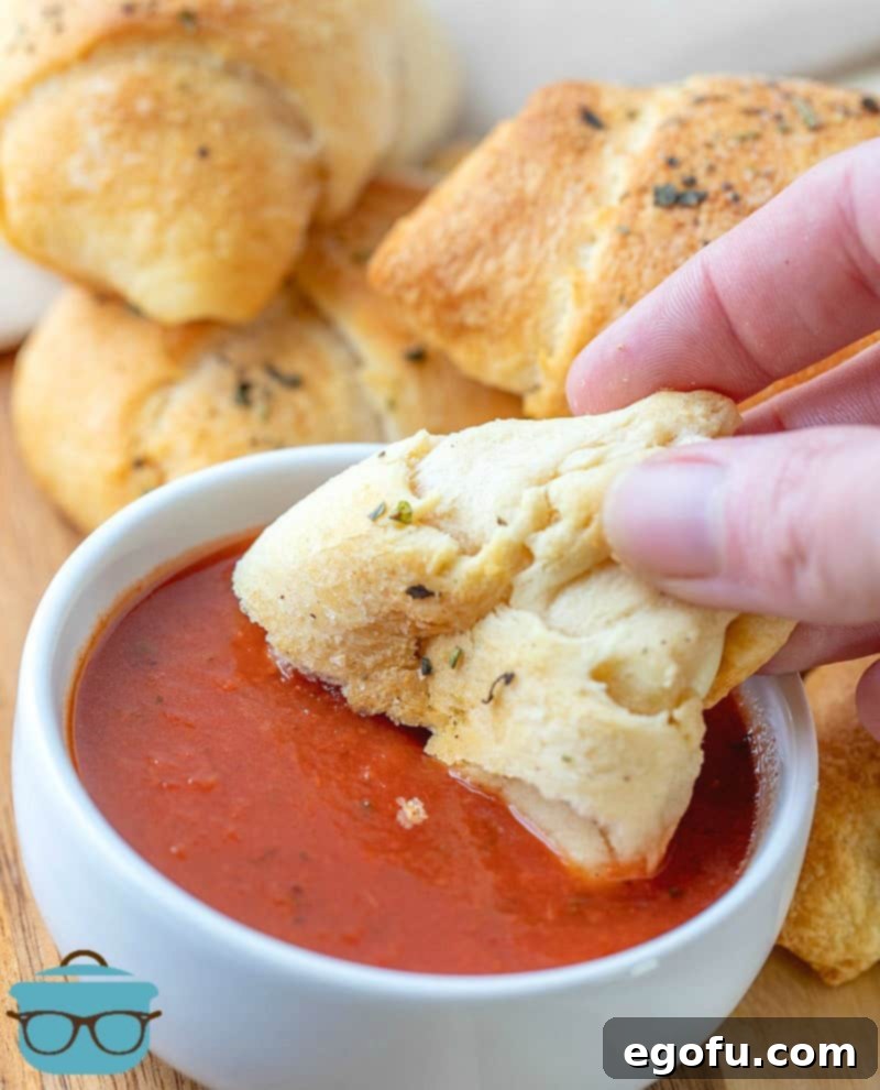 a hand holding a Pepperoni Roll Ups dipped into pizza sauce.