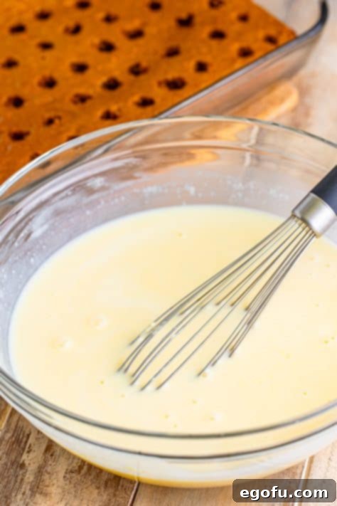 Super Moist Carrot Poke Cake 13 A whisk in a bowl of cheesecake pudding.