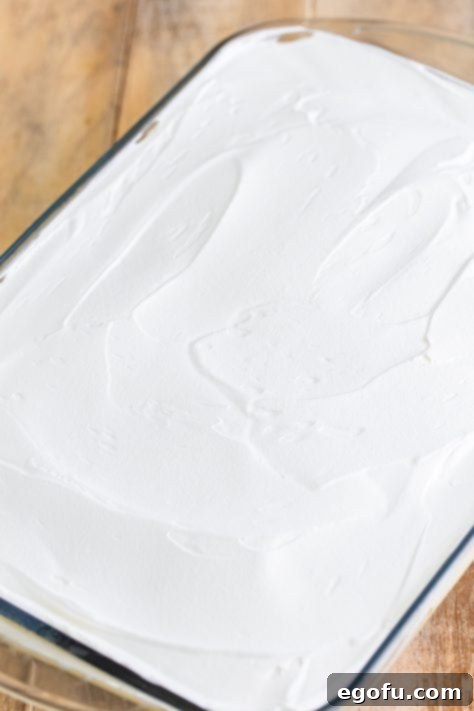 Super Moist Carrot Poke Cake 15 Whipped topping over a layered pudding and cake cake in a glass baking dish.