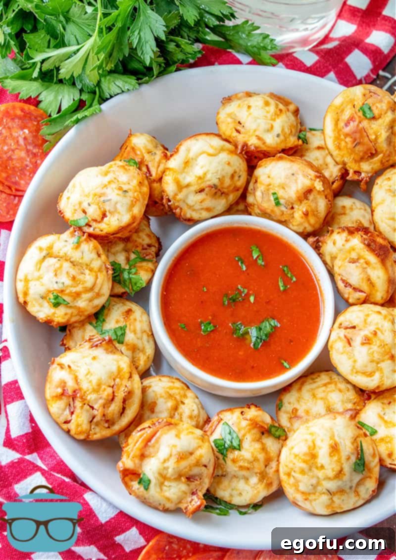 Cheesy Pepperoni Poppers 11 pepperoni pizza puffs shown on a white platter with a small bowl of marinara in the middle of the platter.