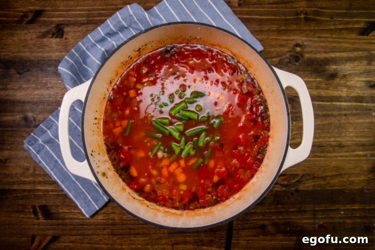 Rotini pasta and frozen green beans added to soup pot and stirred