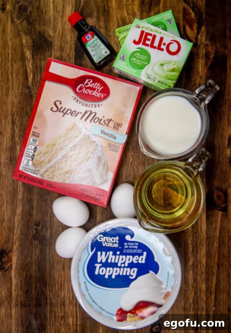 Vanilla cake mix, instant pistachio pudding, large eggs, oil, milk, green food coloring, and whipped topping (Cool Whip) laid out as ingredients.
