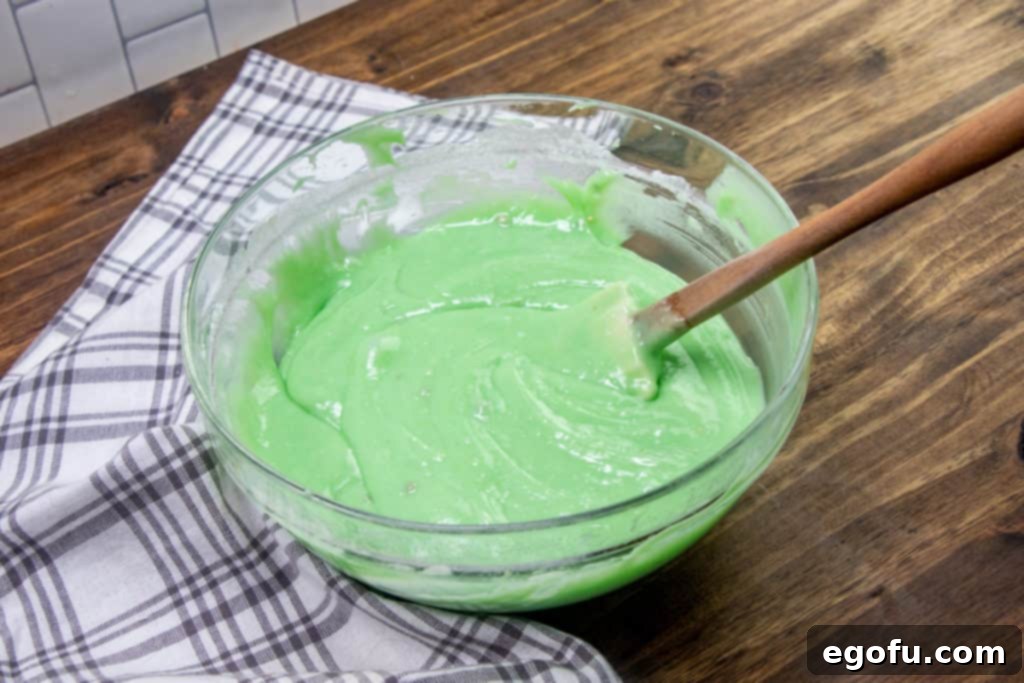 Green food coloring stirred into cake batter in a glass bowl.