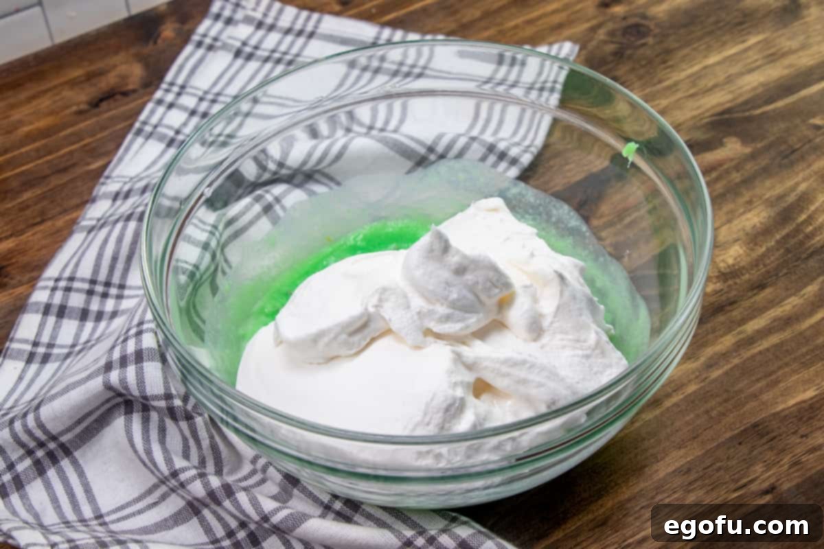 Whipped topping added to pistachio pudding mixture in bowl.