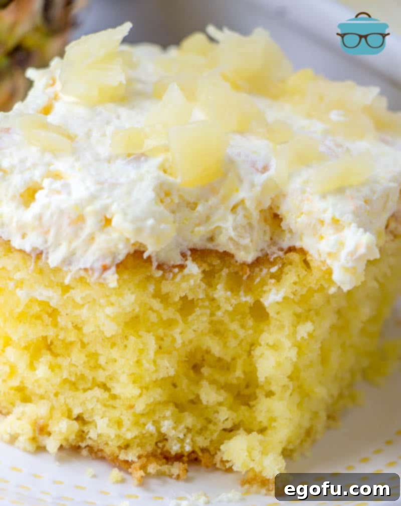 Piña Colada Paradise Poke Cake 2 A closeup photo of a slice of pina colada cake that has had a bite removed, showcasing its moist texture and layers of pineapple, whipped topping, and coconut.