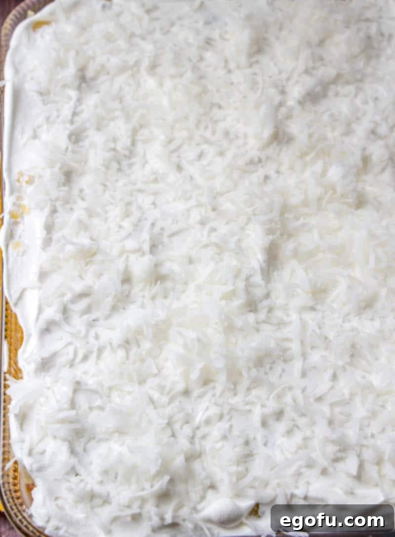 Piña Colada Paradise Poke Cake 11 The finished butter cake topped with the infused glaze, crushed pineapple, a thick layer of whipped topping, and a generous sprinkle of sweetened shredded coconut.