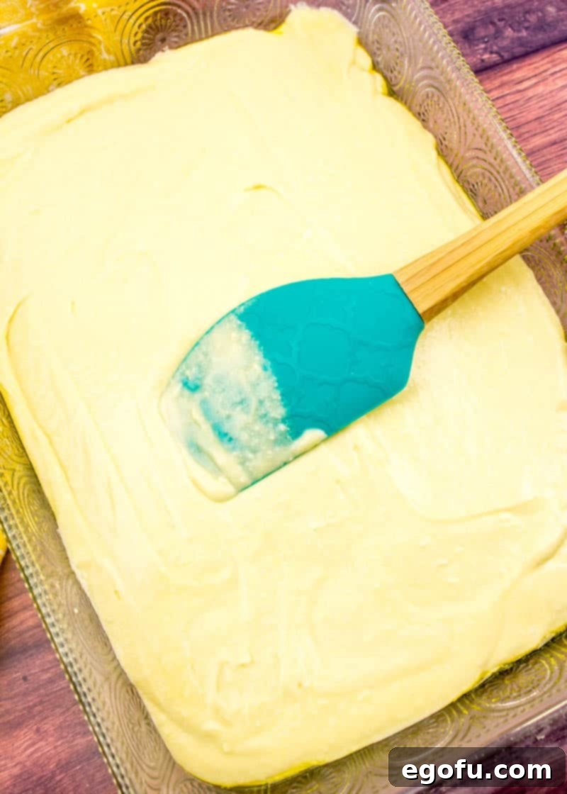 Piña Colada Paradise Poke Cake 6 Butter yellow cake mix batter evenly spread in a 9x13 baking dish, ready for the oven.