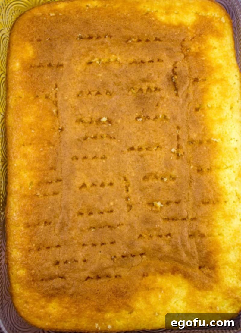 Piña Colada Paradise Poke Cake 8 A baked butter cake mix in a 9x13 baking dish with numerous holes poked into its surface, ready for the liquid glaze.