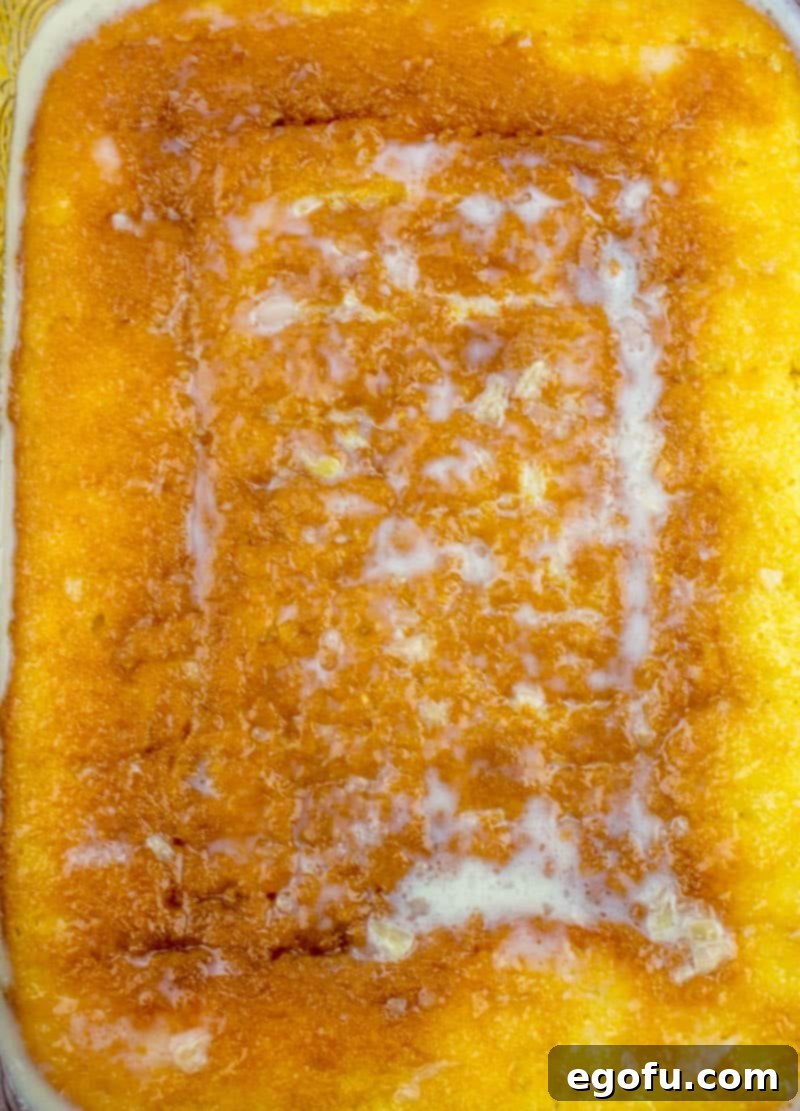 Piña Colada Paradise Poke Cake 9 The sweetened condensed milk, cream of coconut, and pineapple juice mixture being poured into the holes of the warm cake, showing a saturated surface.