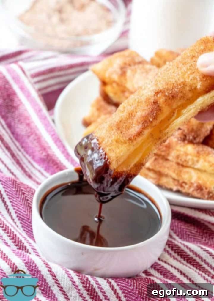 A hand elegantly dipping a golden, baked churro into a rich, dark chocolate sauce, highlighting the perfect pairing of this crispy cinnamon sugar treat with a classic indulgent dip.