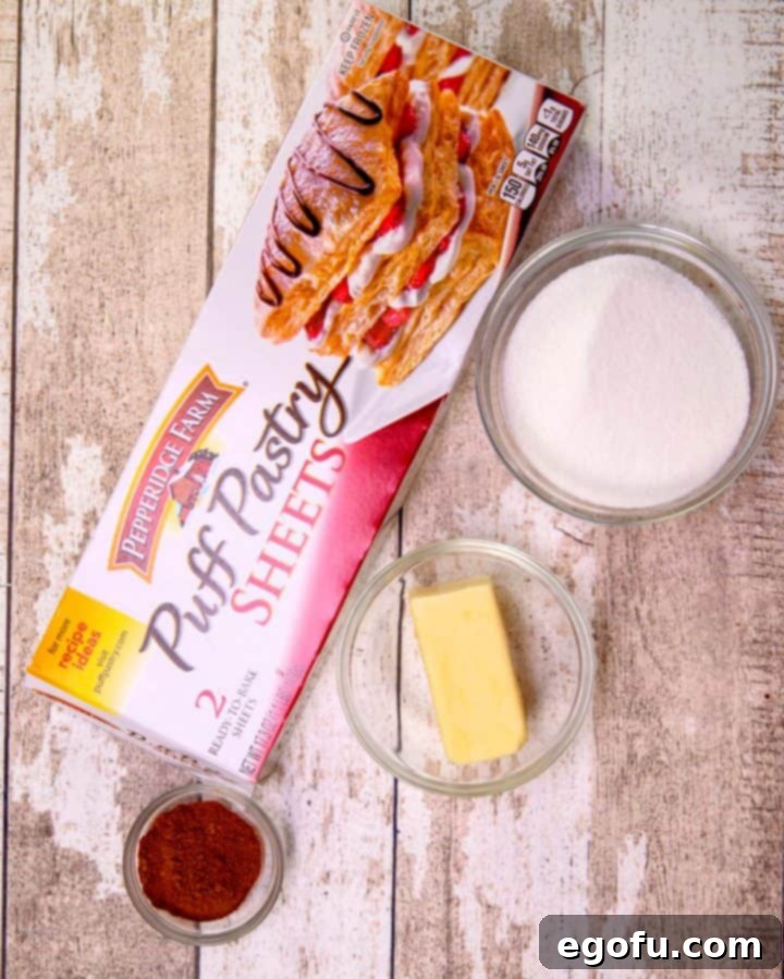A simple yet essential collection of ingredients for homemade baked churros, featuring a box of puff pastry, a stick of unsalted butter, a bowl of granulated sugar, and a small container of ground cinnamon, all neatly arranged on a rustic wooden surface.