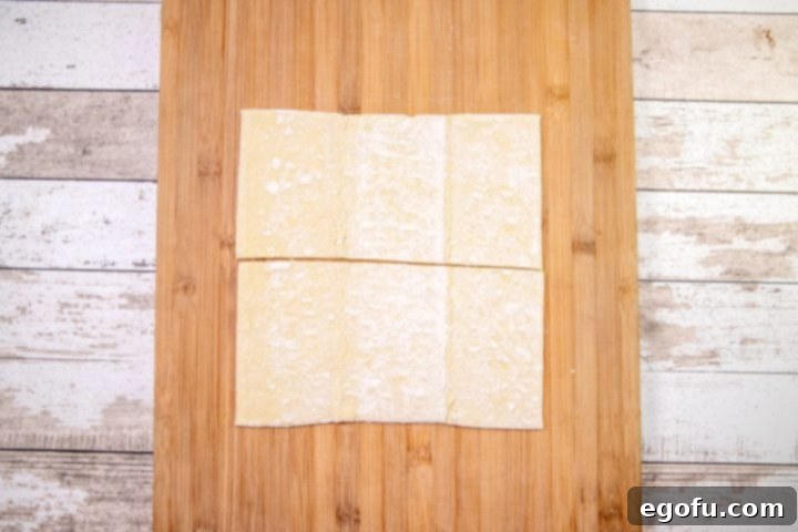 A thawed sheet of puff pastry neatly cut in half horizontally, laid out on a wooden cutting board, ready for the next step in creating baked churros.