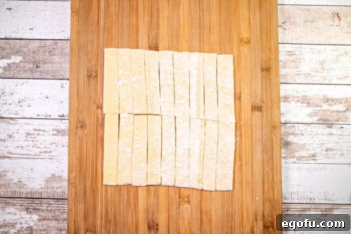 Multiple strips of puff pastry neatly cut and arranged on a wooden cutting board, prepared for baking into easy churros.