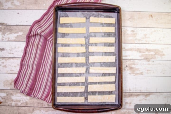 Delicate puff pastry strips neatly arranged in a single layer on a parchment-lined baking sheet, poised for baking into golden, crispy churros.