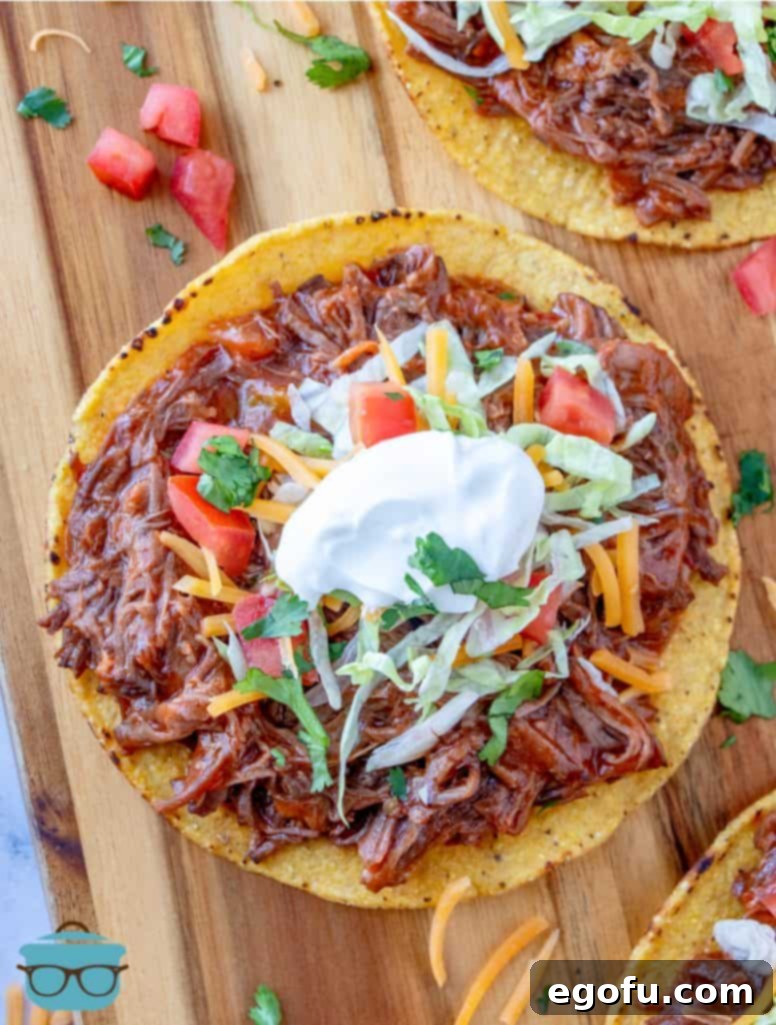 Fiesta-Ready Slow Cooker Shredded Beef 2 A vibrant tostada piled high with Mexican shredded beef, crisp lettuce, and fresh tomato, presented on a rustic wooden cutting board, inviting you to a delicious taco night.