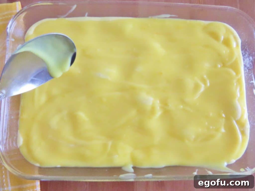 Lemon pudding mixture being spread over lemon cake batter in a baking dish