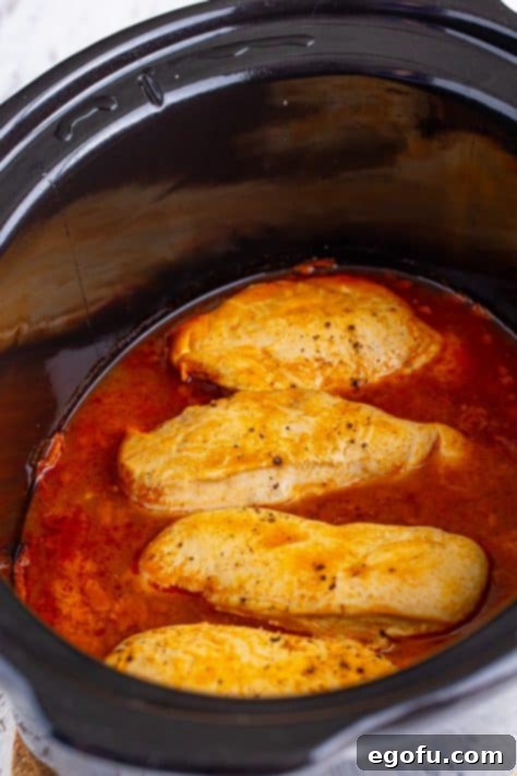A crock pot with cooked chicken and hot sauce.