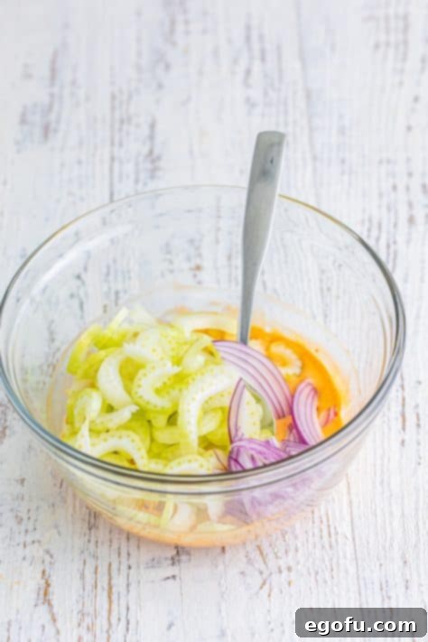 A glass mixing bowl with red onion, buffalo sauce, and celery.