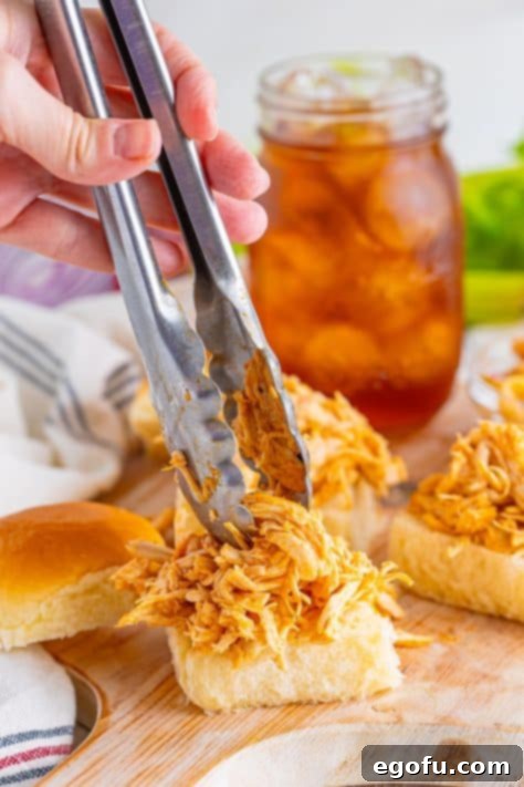 A hand and tongs putting Buffalo Chicken on Hawaiian slider rolls.