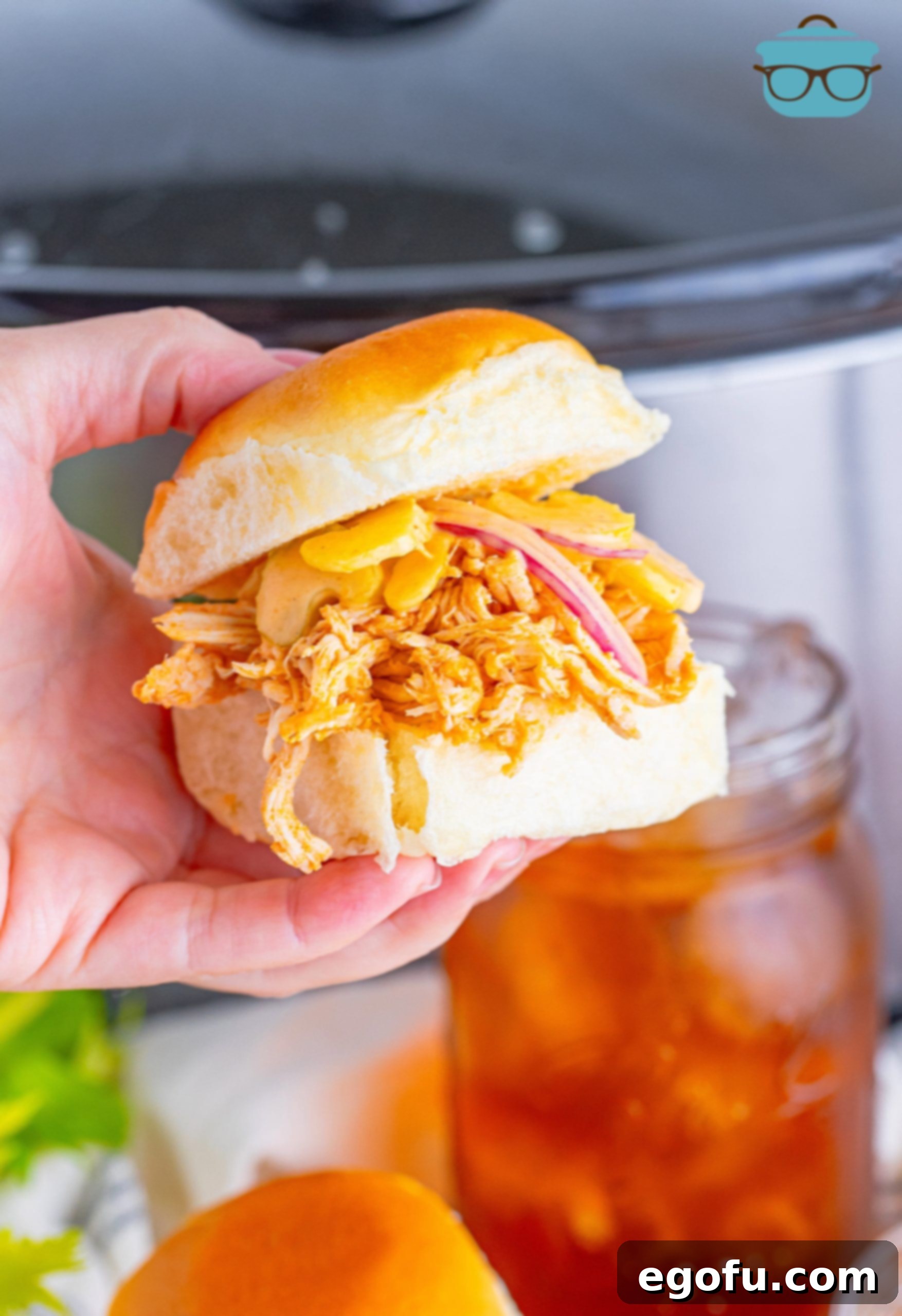 A hand holding a perfectly crafted Crock Pot Buffalo Chicken Slider, showcasing its appetizing layers and inviting texture.
