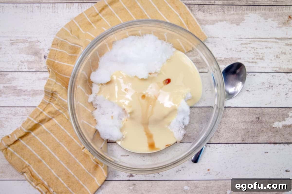 sweetened condensed milk and vanilla extract added to fresh snow in a clear bowl, showing the initial mixing stage.