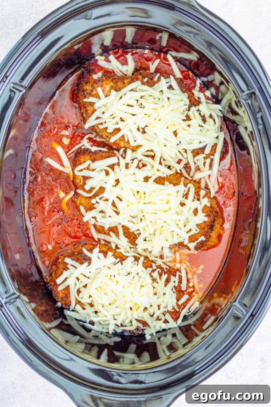 Slow Cooker Chicken Parm Perfection 13 Shredded mozzarella cheese being added to cooked chicken breasts in the slow cooker, about to melt.