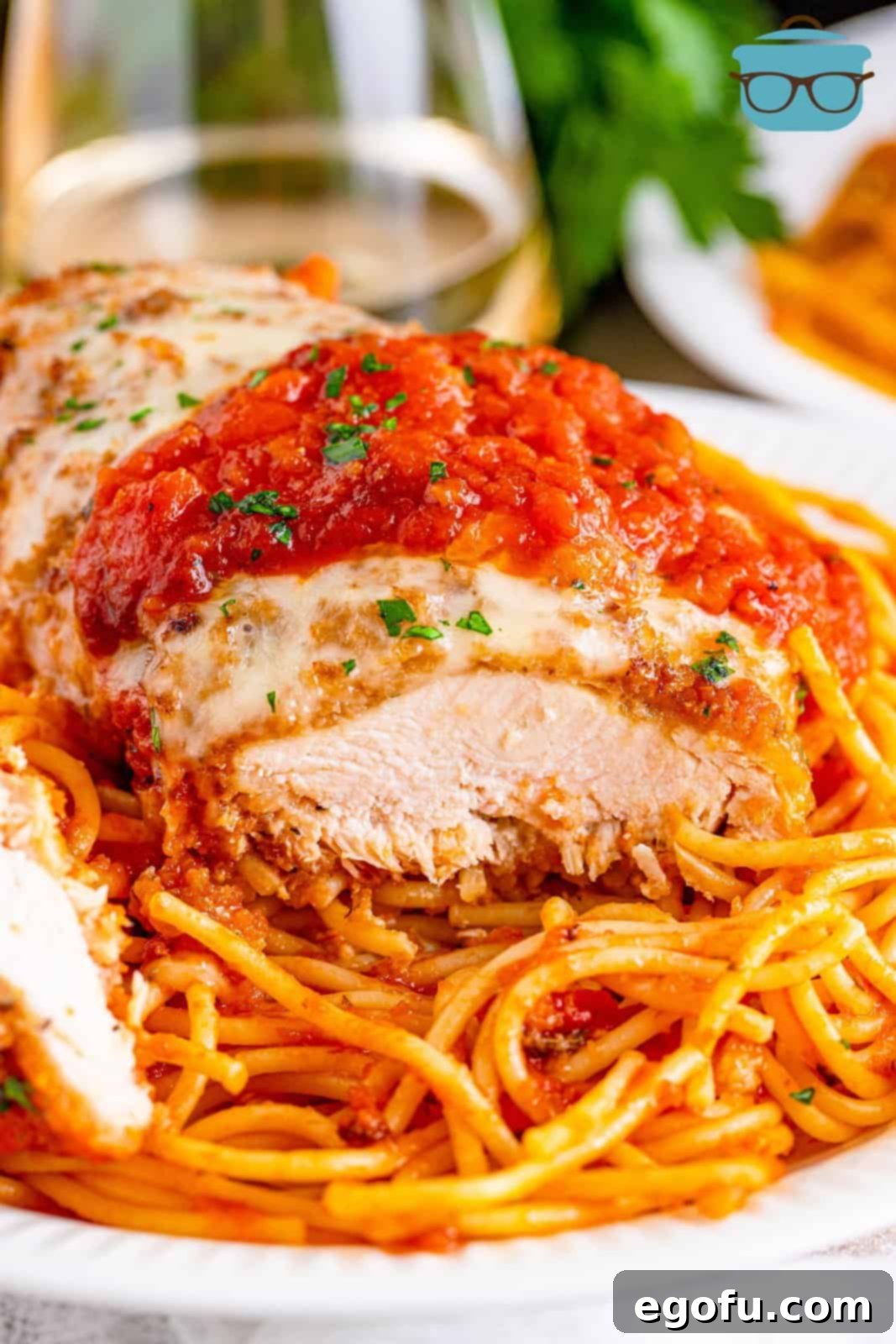 Slow Cooker Chicken Parm Perfection 15 A serving of sliced chicken breast over a bed of spaghetti with sauce and melted cheese, garnished with fresh herbs.