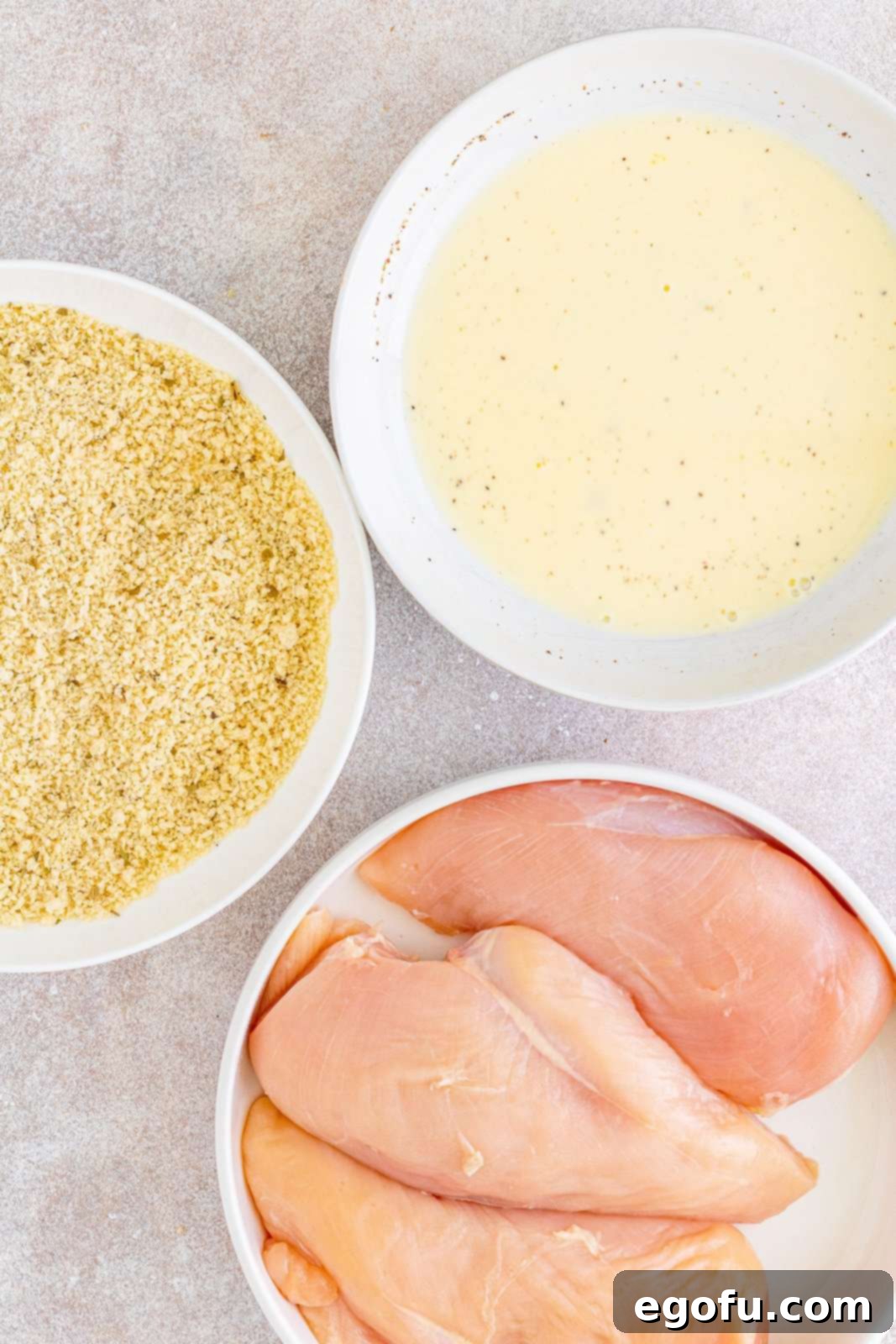 Slow Cooker Chicken Parm Perfection 9 An assembly line setup showing a bowl of raw chicken, a bowl with the egg/milk mixture, and a bowl with panko bread crumbs.