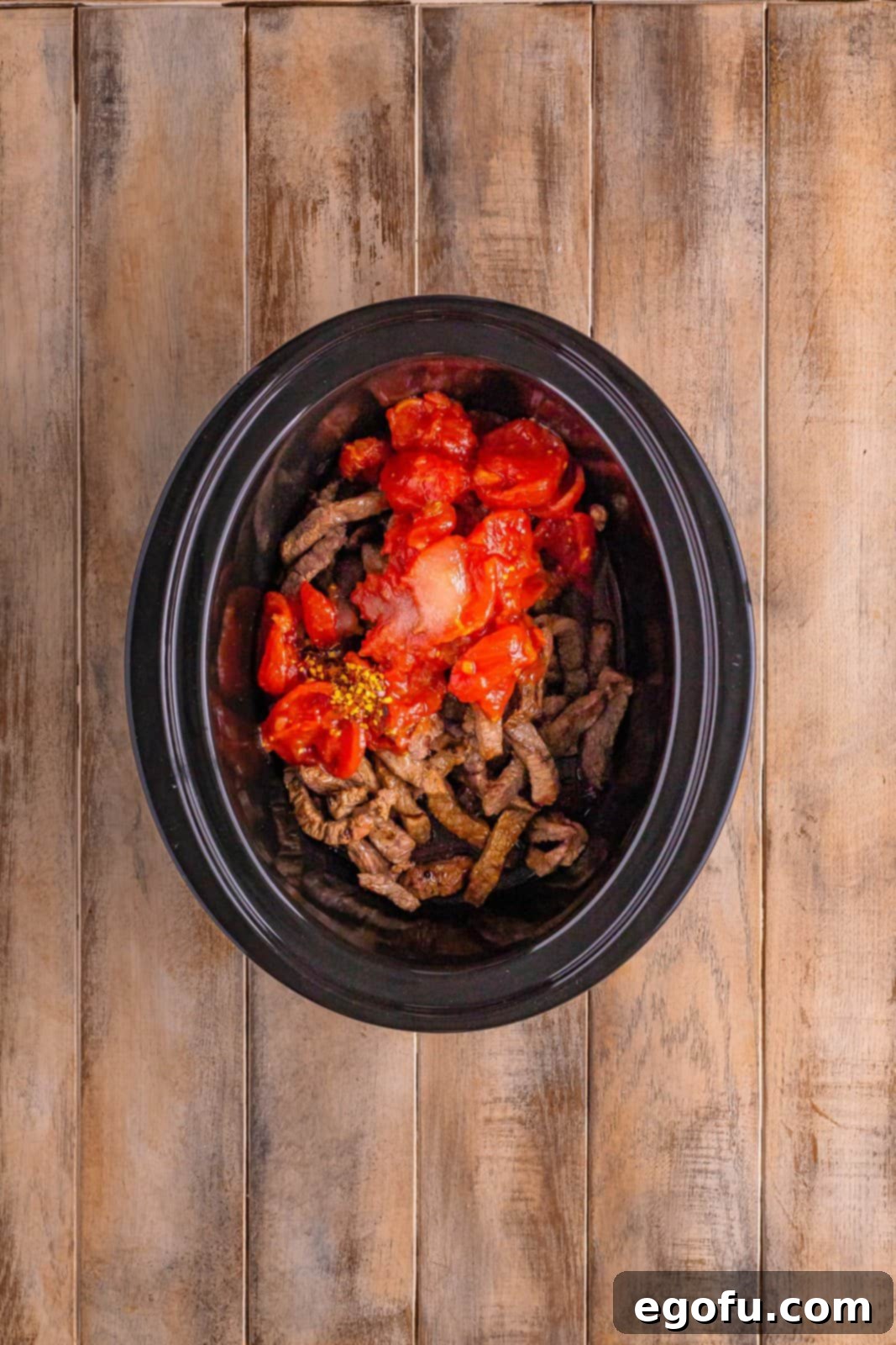 Slow Cooker Pepper Steak 10 Stewed tomatoes and red pepper flakes added on top of the seared pepper steak in the black oval slow cooker.