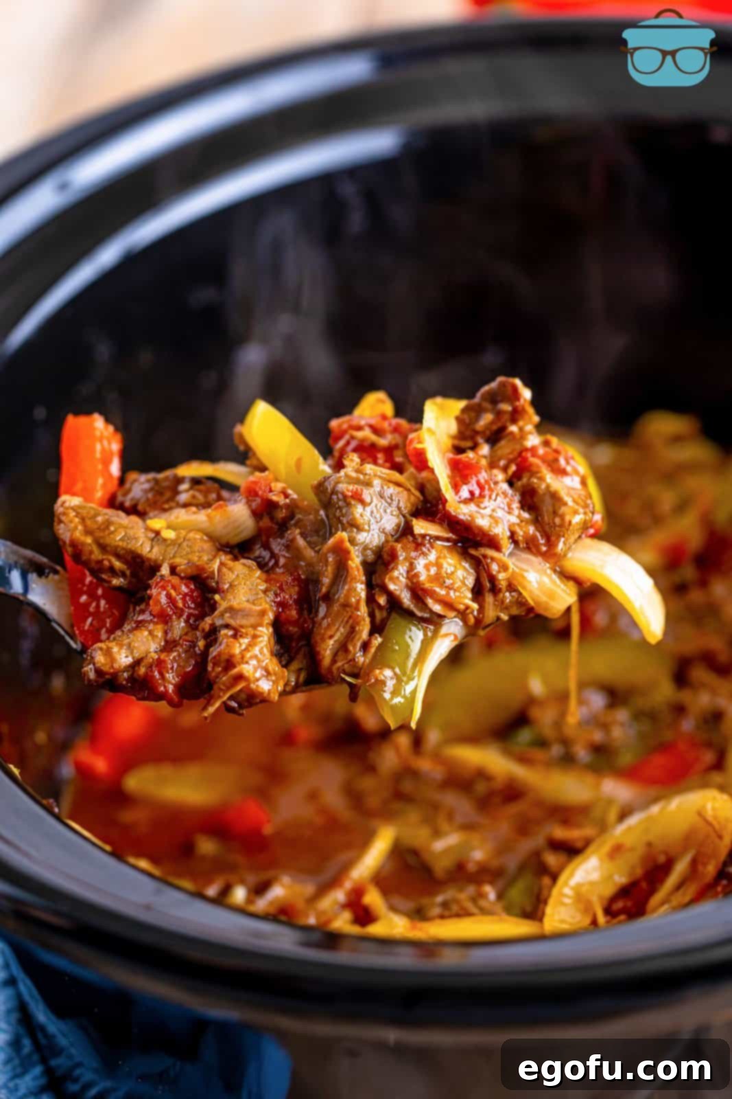 Slow Cooker Pepper Steak 12 A large spoon lifting a portion of cooked pepper steak, showcasing the tender beef and softened peppers, over the slow cooker.