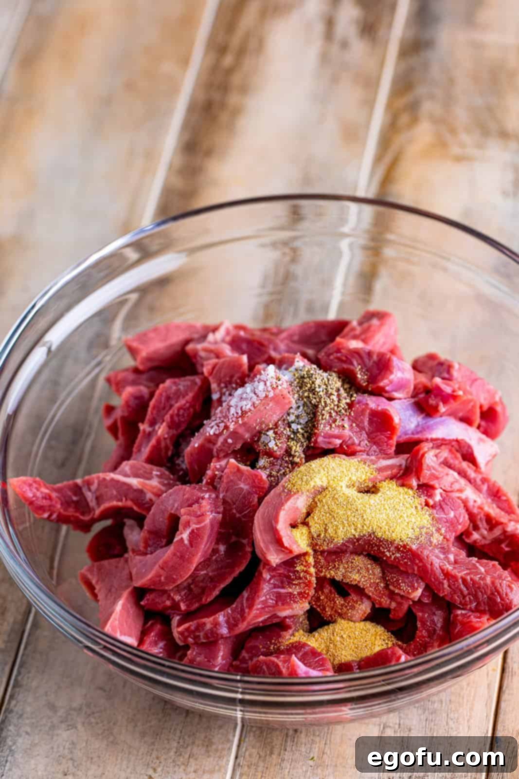 Slow Cooker Pepper Steak 5 Sliced steak strips seasoned with salt, pepper, and garlic powder in a bowl, ready for browning.