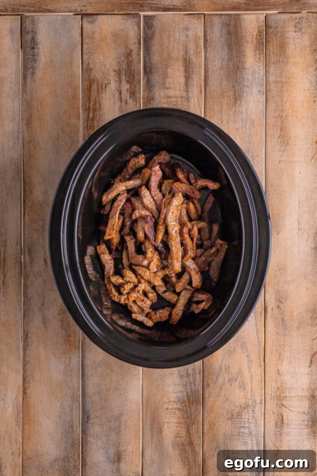 Slow Cooker Pepper Steak 7 Browned beef strips placed inside a black, oval slow cooker, ready for the sauce.