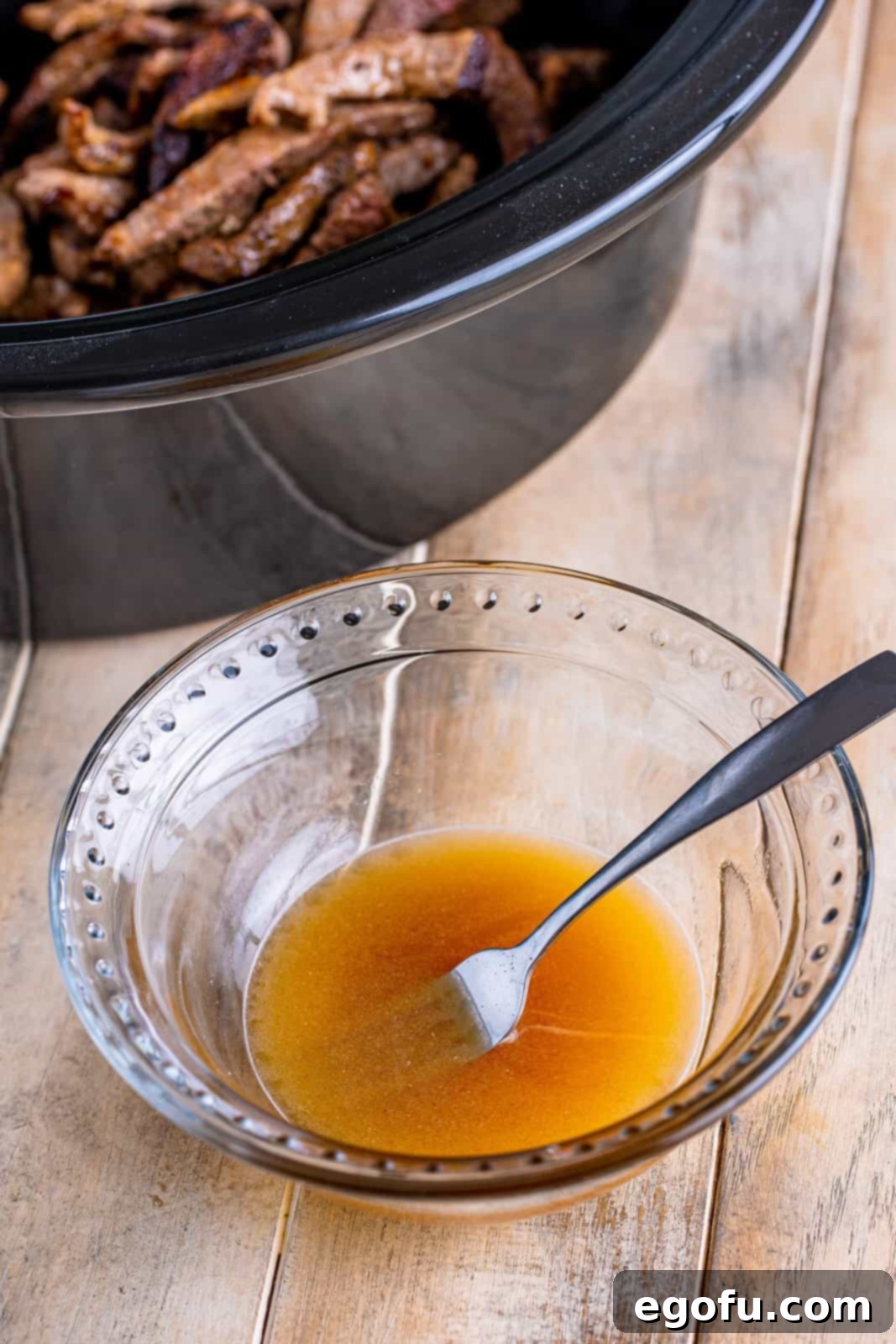 Slow Cooker Pepper Steak 8 A crushed beef bouillon cube mixed with hot water in a small clear bowl with a fork, dissolving.