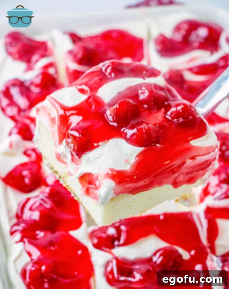 Ruby Snowdrift Cake 2 A spatula lifting a perfect slice of Cherries in the Snow Poke Cake from the pan, showcasing its beautiful layers of white cake, creamy pudding, and vibrant cherry topping.